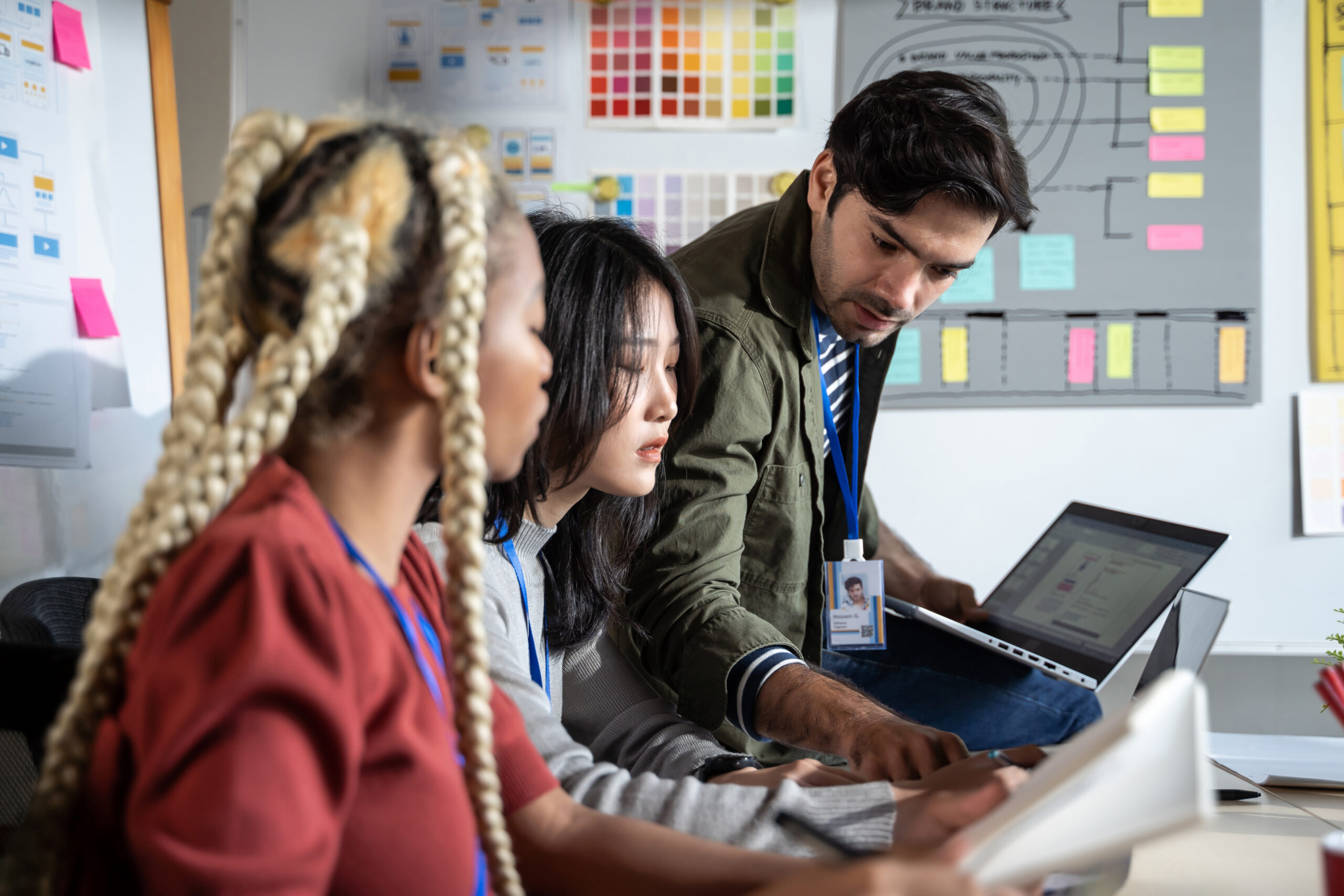A diverse team of website developers collaborating over laptops at a desk with design wireframes and color swatches in the background.