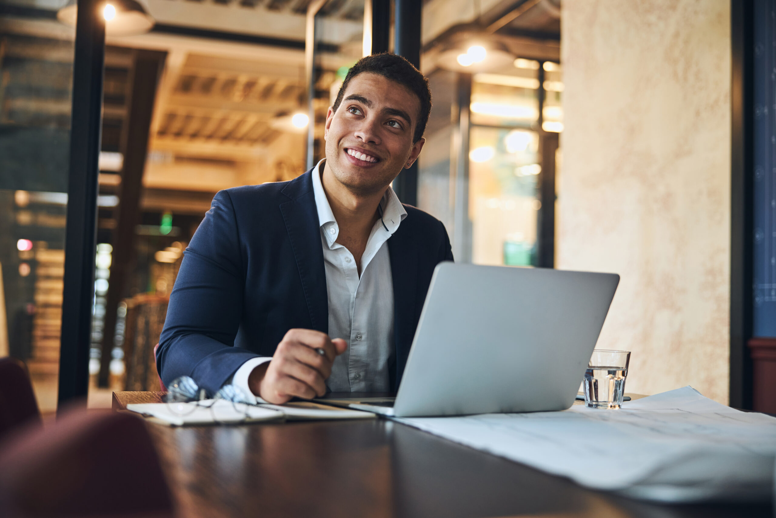 A smiling WP Engine developer working at a dark wooden desk with a laptop in a modern, well-lit office space.