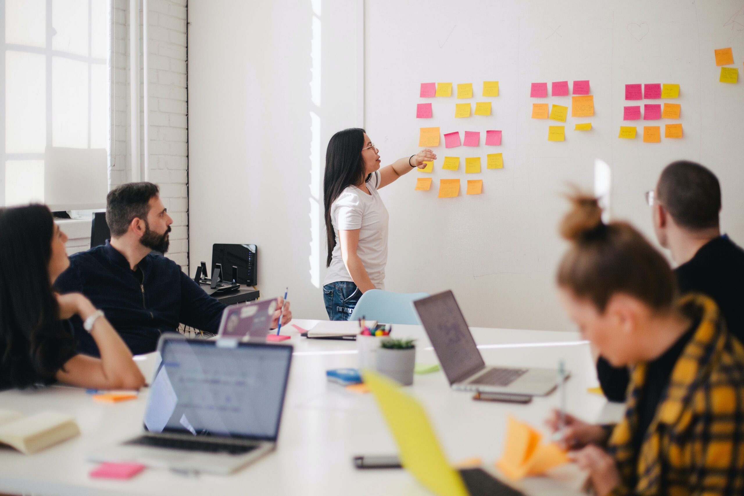 A digital marketing team collaborating during a social media management session as a woman presents content ideas on a whiteboard covered in colourful sticky notes.